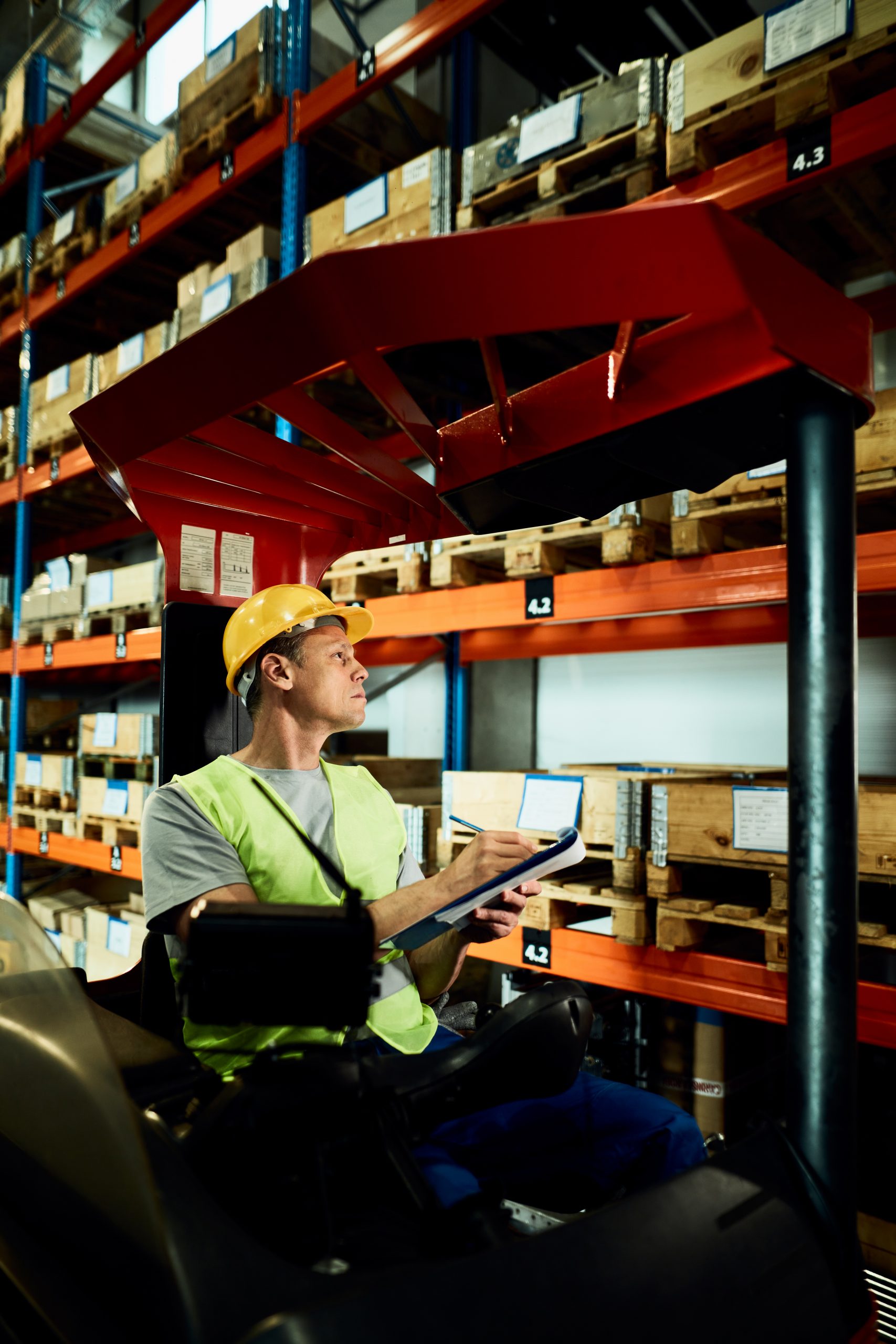 Warehouse worker in a forklift writing notes while checking stoc